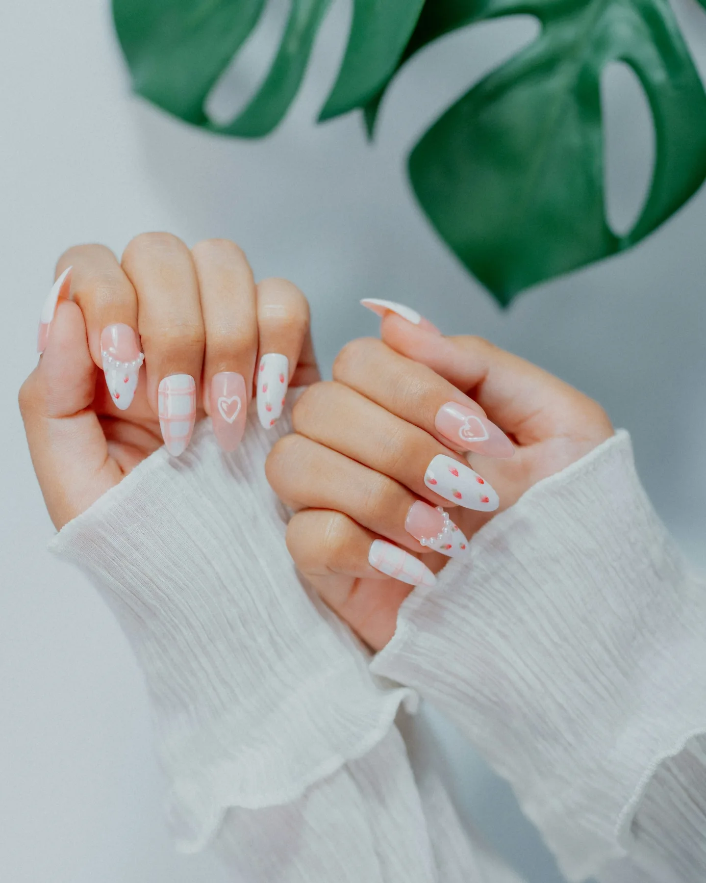 Hands with pink heart nail art beside a monstera leaf