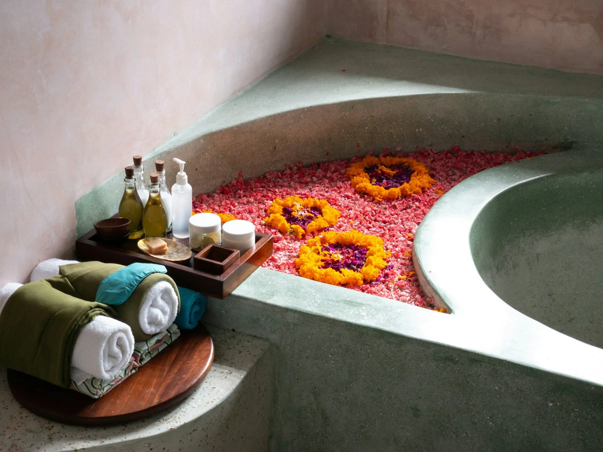 A spa bath filled with flower petals beside folded towels